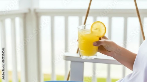 Hand holding refreshing orange juice with lemon on a sunny day.
