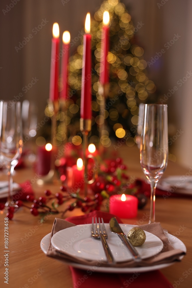 Naklejka premium Stylish Christmas table setting with plates, glasses and burning candles in festive decorated room, closeup. Bokeh effect