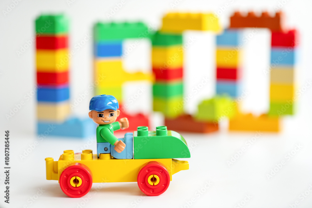 Naklejka premium A Lego construction worker sits on a toy car in front of Lego bricks