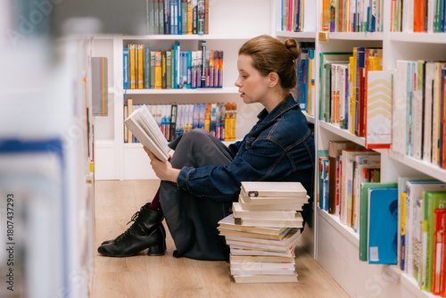 woman sits at shelves in library and reads book. education, scientific work. business person, university lecturer. young Caucasian woman is getting education.