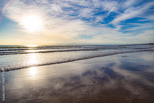 Fototapeta Naklejka Na Ścianę i Meble -  Minimalist seascape with mirror-like wet sand reflecting the sky and a glowing sunbeam on the sea. A serene and peaceful beach scene with incoming surf. Mediterranean coast, Turkey.

