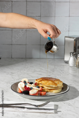 hand pouring syrup on pancakes in hard light