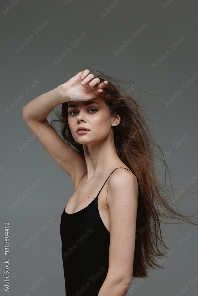 Naklejka premium thoughtful woman posing with flowing hair in black dress against gray background, stylish beauty, serene mood