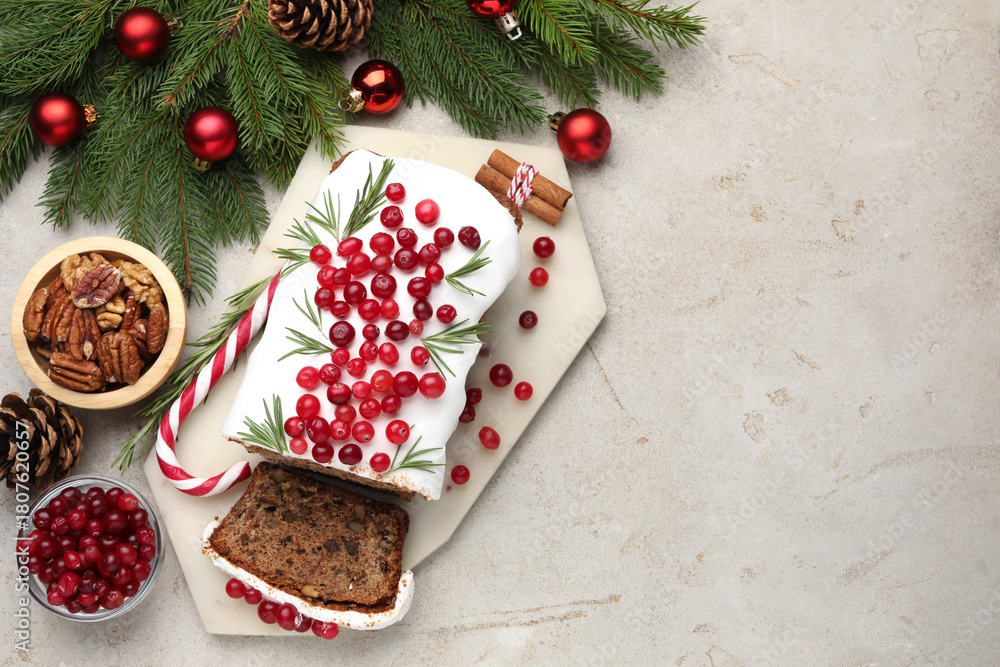 Fototapeta premium Tasty Christmas cake with icing, cranberries, nuts and festive decor on light grey table, flat lay. Space for text