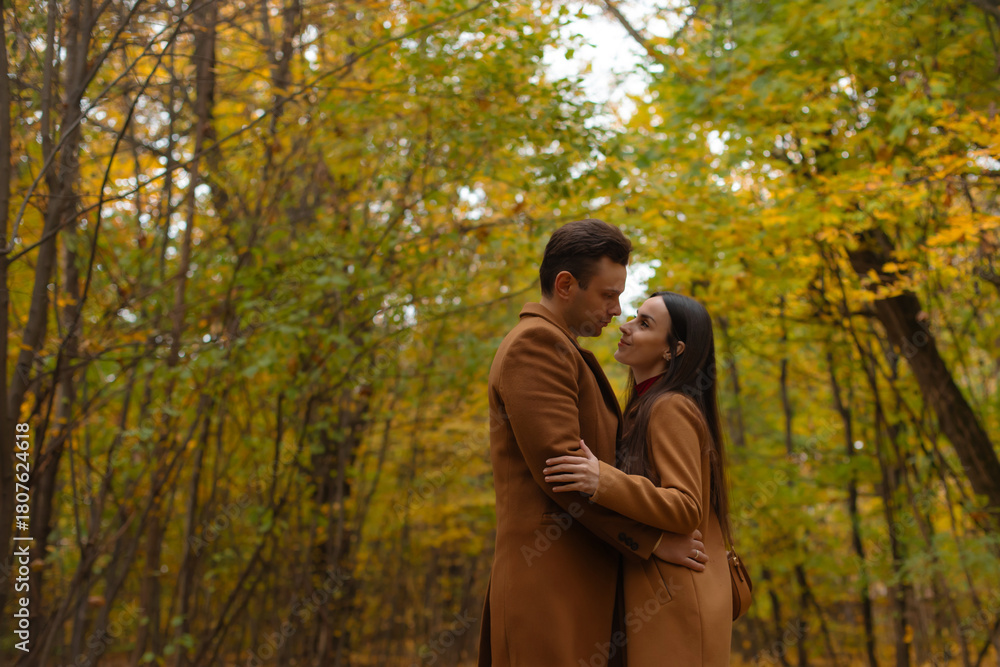 Fototapeta premium Romantic couple embracing in an autumn forest, looking into each other’s eyes. Warm, intimate moment perfect for Valentine’s Day, love, and relationship themes.