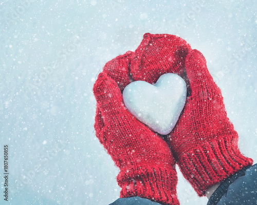Hands in knitted mittens with heart of snow in winter day. Love concept. Valentine day background.	