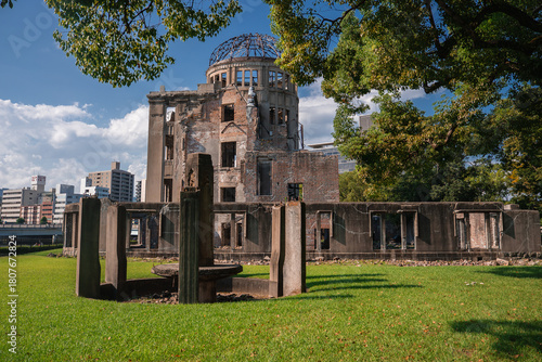 Hiroshima Peace Memorial in Hiroshima, Japan shows the preserved dome and ruins, a circular stone installation with pillars, open lawn, and city buildings beyond.