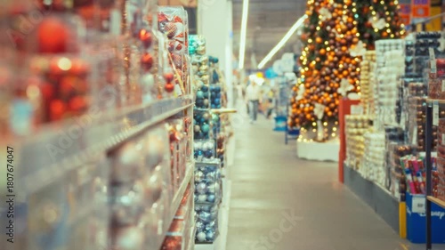 Shoppers wander through a brightly lit store aisle during the holiday season. Colorful decorations adorn the shelves, and a large tree stands at the end of the aisle