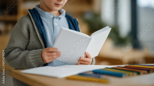 Child holding open blank white book near crayons and markers on a table — concept of children’s book design, creativity, and art education mockup photography. cinematic color correction, natural