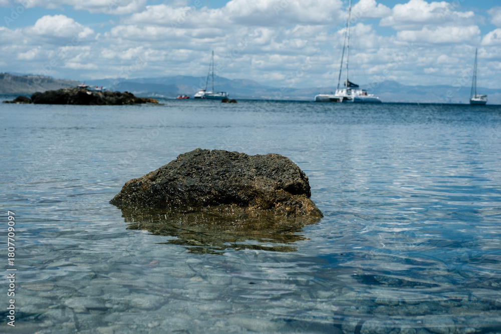 Fototapeta premium Tranquil coastal view with sailboats and rocky shore under cloudy sky
