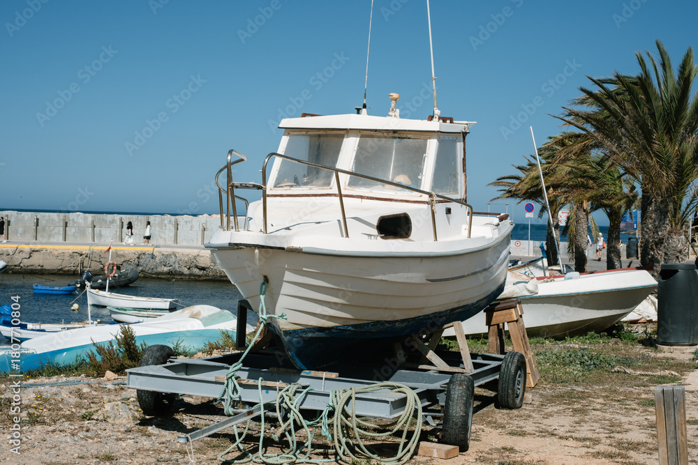 Fototapeta premium Vintage boat on trailer at sunny coastal harbor with palm trees