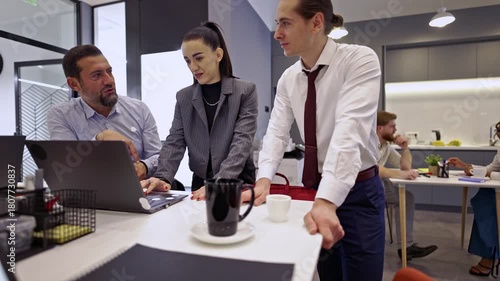 Engaged business colleagues work together, reviewing data on a laptop and exchanging thoughts. This dynamic team collaborates effectively in a contemporary office setting.