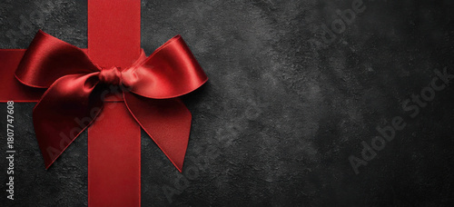 A shiny red satin ribbon and bow tied around a gift on a dark, textured grunge background with copy space.