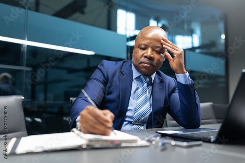 Фотография Mature African American businessman taking notes while thinking deeply at his of