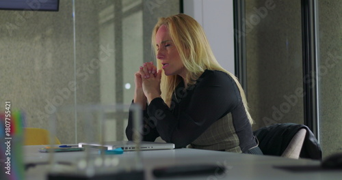 Business woman resting head on arms while seated at desk, appearing mentally drained and emotionally withdrawn in quiet office environment