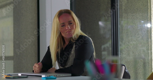 Business woman resting head on arms while seated at desk, appearing mentally drained and emotionally withdrawn in quiet office environment