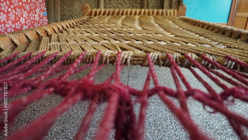 Close-up macro of a woven rattan chair seat with burgundy red fringe trim, texture concept.