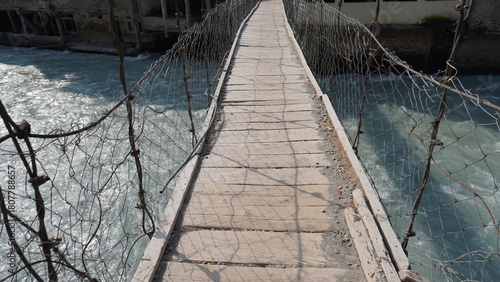 Weathered wooden suspension bridge walkway stretching across a turbulent blue river, crossing concept.