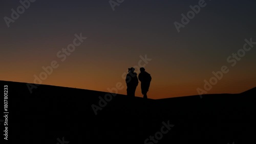 Two Berber men walking in silhouette during a warm Sahara Desert sunset.