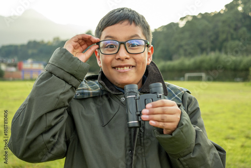 Mexican boy exploring nature with binoculars, smiling wearing glasses outdoors