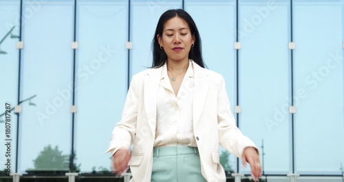 Serious portrait video of a young Asian businesswoman looking directly at the camera with crossed arms in a modern urban setting.