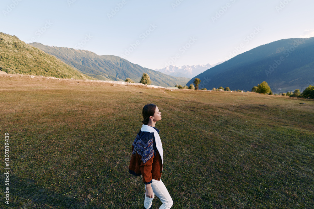 Fototapeta premium Woman walking in a mountain meadow, hiking with a backpack across open landscape and nature scenery, enjoying solitude and fresh air during outdoor exploration.