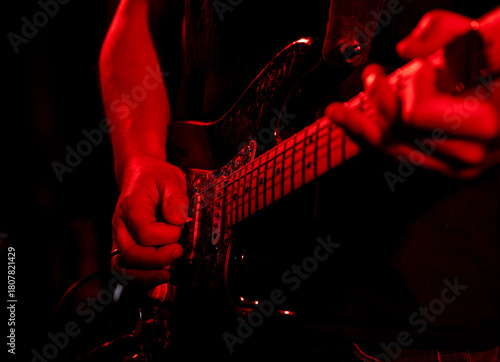 Young male guitarist playing electric guitar under red stage lights