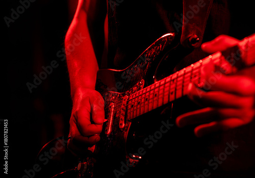 Close-up of guitarist playing electric guitar on stage in red lighting