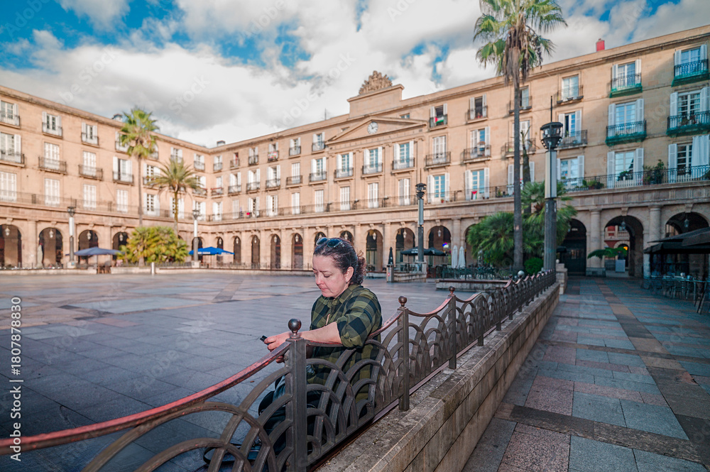 Naklejka premium Woman looking at phone in Plaza Nueva Bilbao