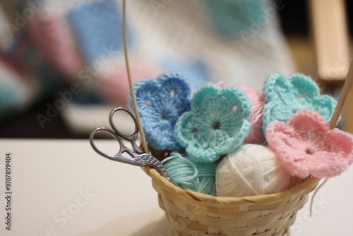 Basket with clews balls wool yarn and crocheted flowers handmade in the living room. blanket, shelves books clock photo cozy home handmade	
