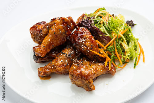 Glazed chicken wings with sesame and fresh slaw on white plate, studio top view