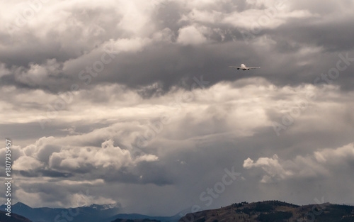 Commercial airplane ascending into dense, overcast clouds after taking off from Jackson Hole Airport in Jackson, Wyoming. The sky is filled with dramatic, dark gray clouds, creating a moody atmosphere