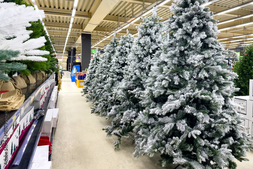 A row of green undecorated artificial Christmas trees in shopping mall or warehouse. Store of Christmas symbols and accessories. Preparation for New year