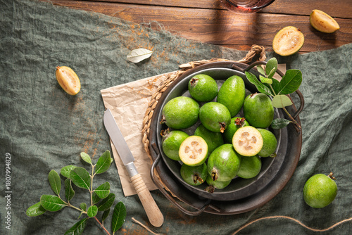 Overhead shot of a rustic still life with ripe pineapple guavas, some cut open to reveal the fleshy pulp, on a small plate and in a basket