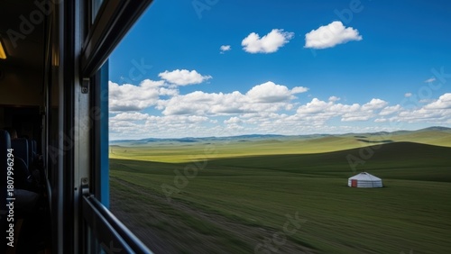 A view of a vast, green Mongolian steppe with a single yurt, seen from a train window.