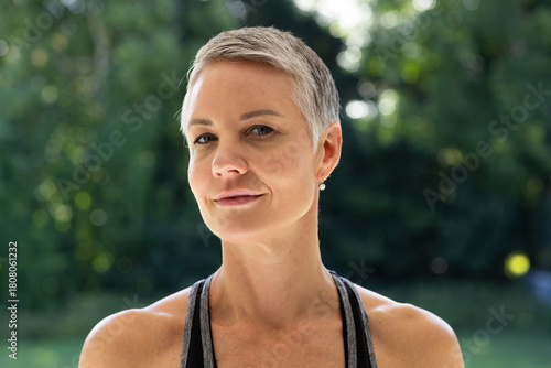 Mature woman sporting pixie haircut and pearl earrings wearing athletic tank posing in garden