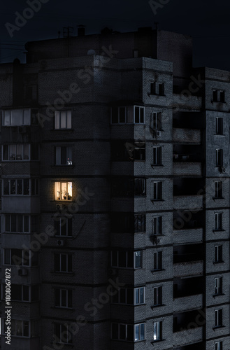 Single brightly lit window on a dark apartment building in Ukraine during power cut