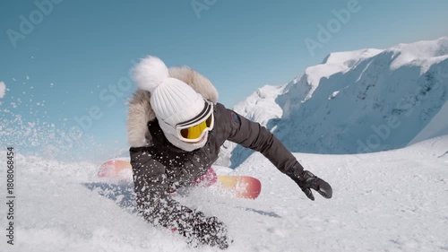 SLOW MOTION, CLOSE UP: Female snowboarder tumbles into soft snow on a sunny alpine slope as she tries to learn to carve on a snowboard. Snow flies toward the camera while she crashes with a smile.