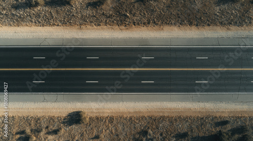 Aerial top down view empty highway asphalt road cracked pavement double yellow line dry roadside barren landscape sunny light high angle solitude transportation