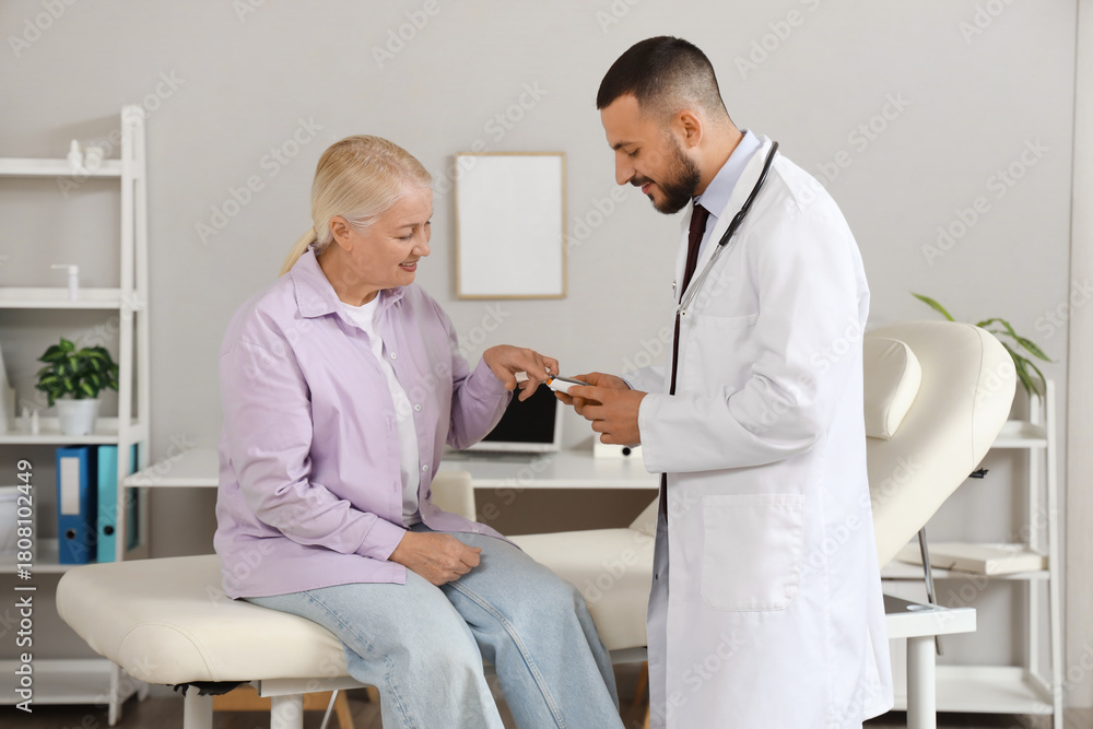 Obraz premium Male doctor with mature woman using glucometer in clinic