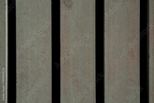 Close up vertical gray metal bars with rust texture and dark gaps, industrial steel background.