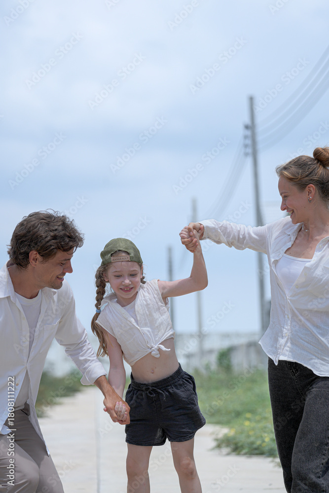 Obraz premium A happy young family holding hands while walking through a new residential neighborhood. The loving parents smile at their daughter, enjoying a peaceful stroll and quality time together.