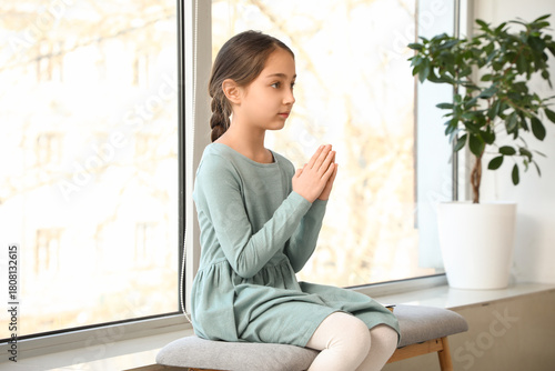 Free Download Little girl sitting on bench and praying near window at home - GFXLoad