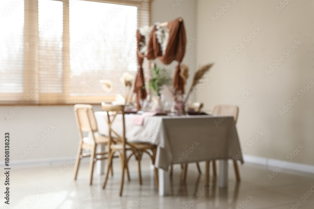 Fototapeta premium Blurred view of elegant table setting with beautiful flowers and draped fabric decor in stylish dining room