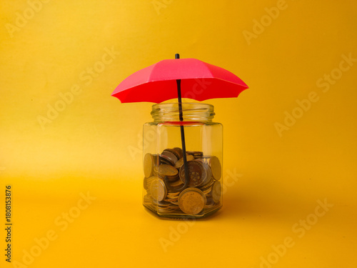 The concept of financial security or insurance by showing coins in a jar protected by an umbrella