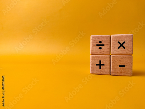 The image displays four wooden blocks with basic mathematical operation symbols on a yellow background
