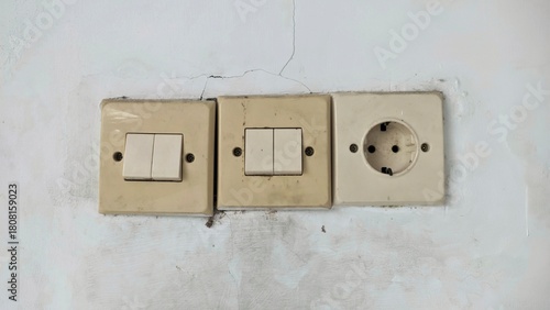 Old, dirty light switches and power socket on a cracked, poorly maintained house wall.
