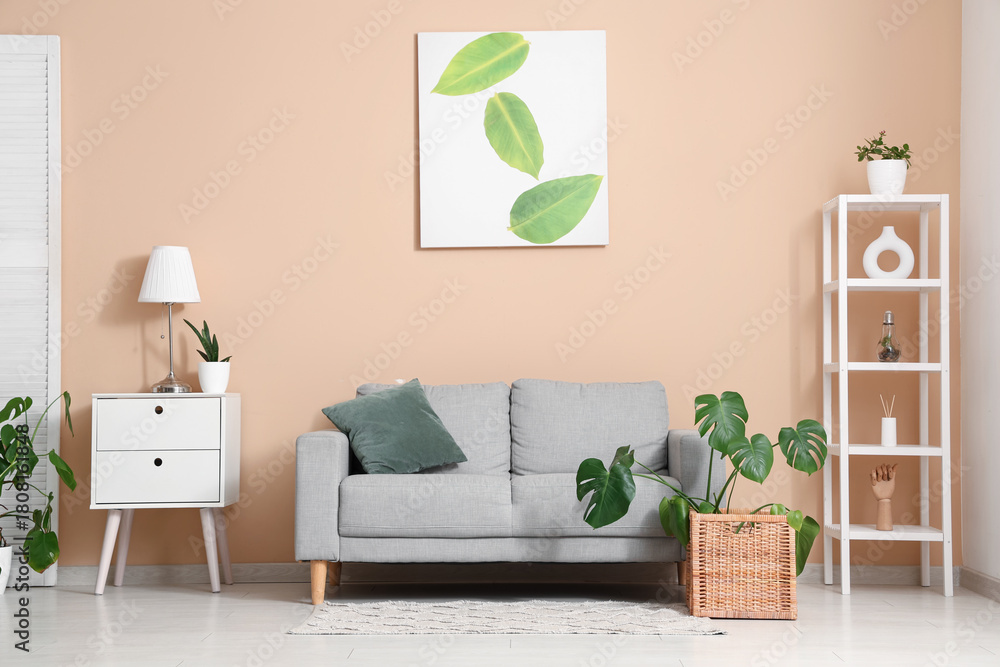 Naklejka premium Interior of living room with sofa, shelving unit and Monstera houseplant near beige wall