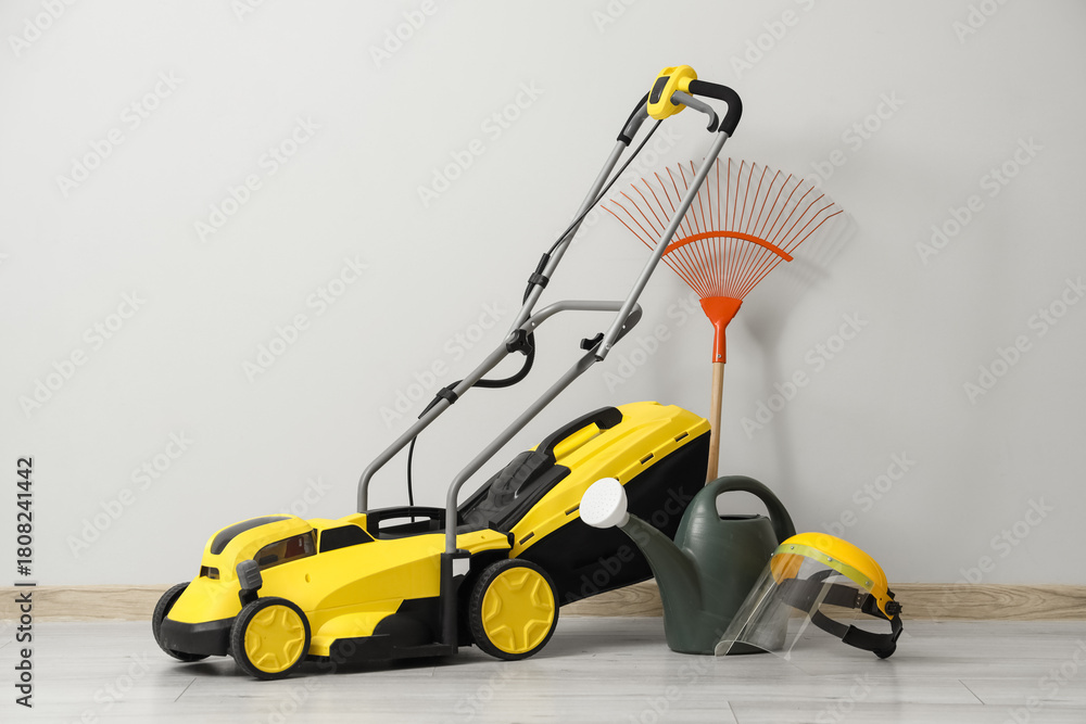 Fototapeta premium Lawn mower with gardening tools near light wall in room