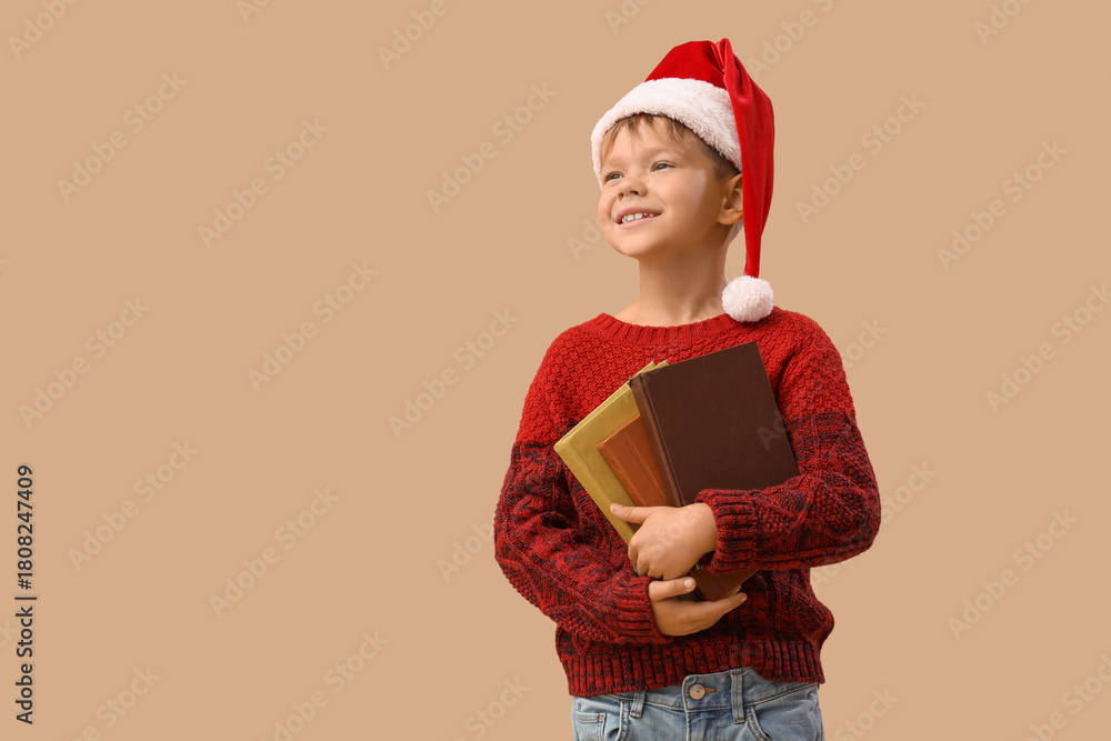 Naklejka premium Cute little boy in Santa hat with books on beige background